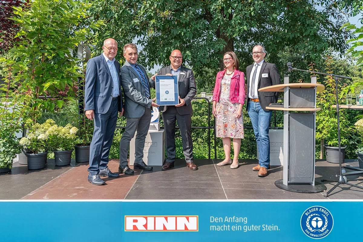 Four men and a woman hold a certificate up to the camera. Underneath is the slogan: RINN, A good stone makes the beginning.