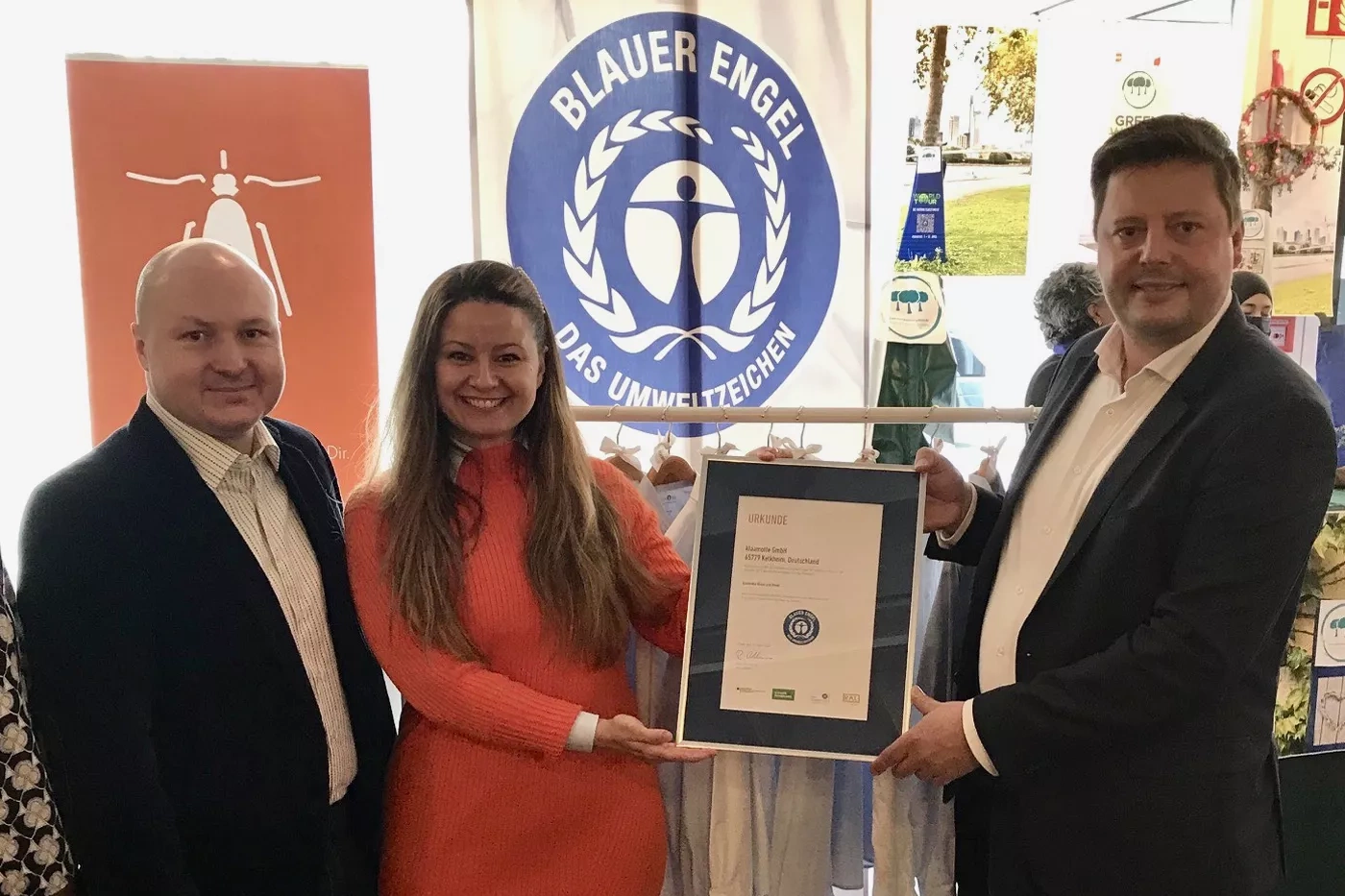 A man and a woman hold the certificate together with Christoph Eßer-Ayertey. 